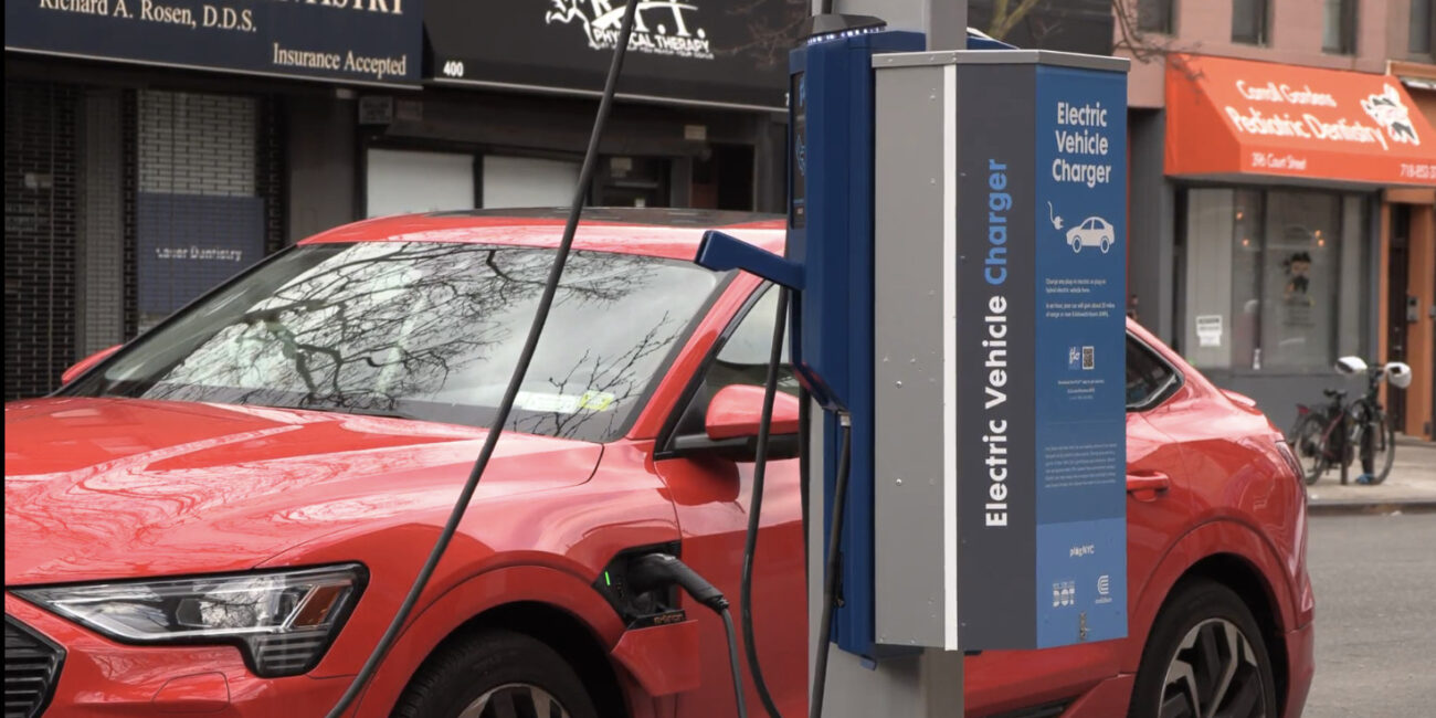 A red electric car is shown at a charging station in Manhattan.