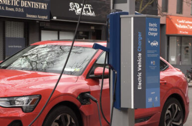 A red electric car is shown at a charging station in Manhattan.