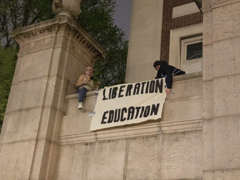 Two protestors put up a banner at Hamilton Hall after they occupied the building. (Credit: Indy Scholtens)