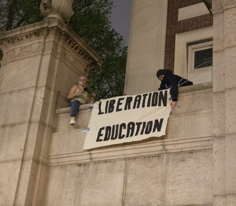 Two protestors put up a banner at Hamilton Hall after they occupied the building. (Credit: Indy Scholtens)