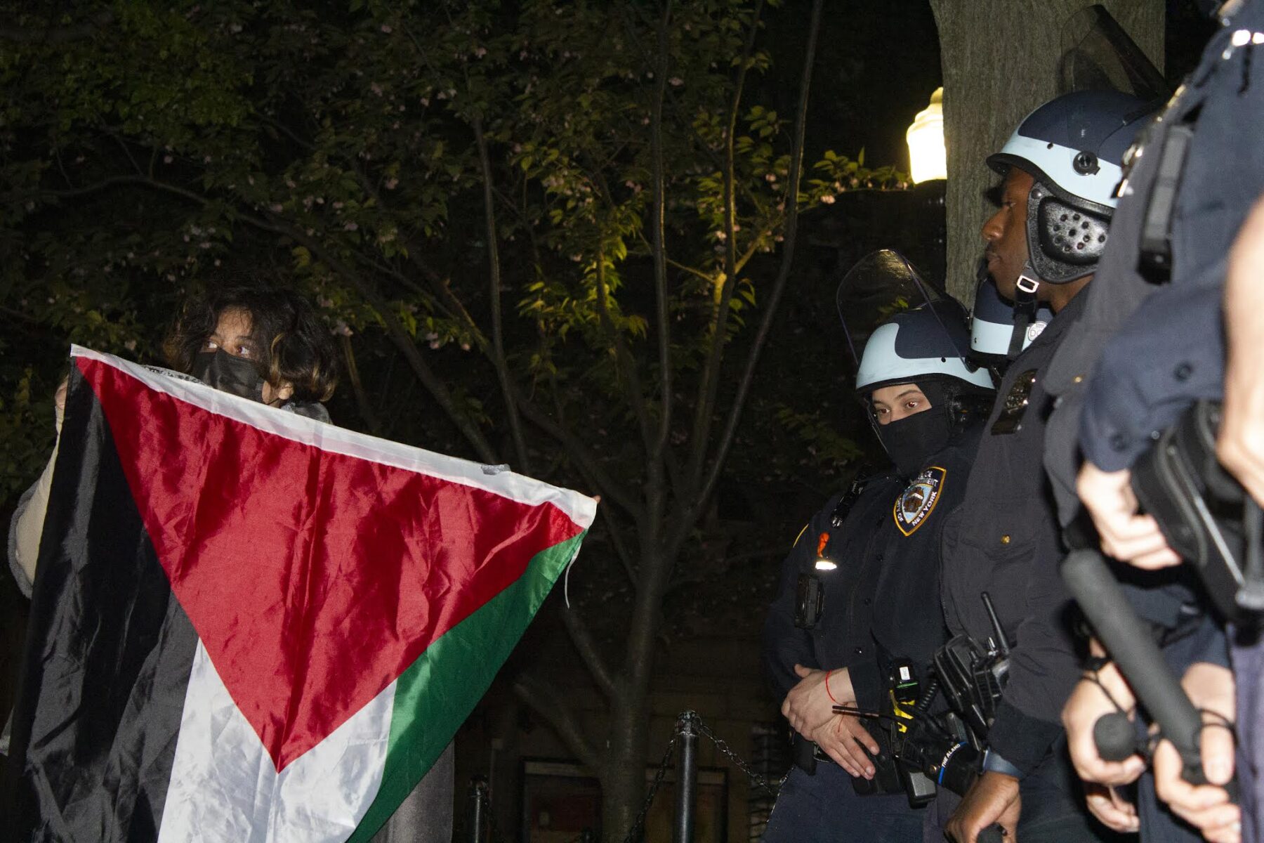 A protester holds the Palestinian flag aloft in front of NYPD officials on Tuesday, April 30, 2024 inside the Columbia University campus.(Credit: Uzma Afreen)