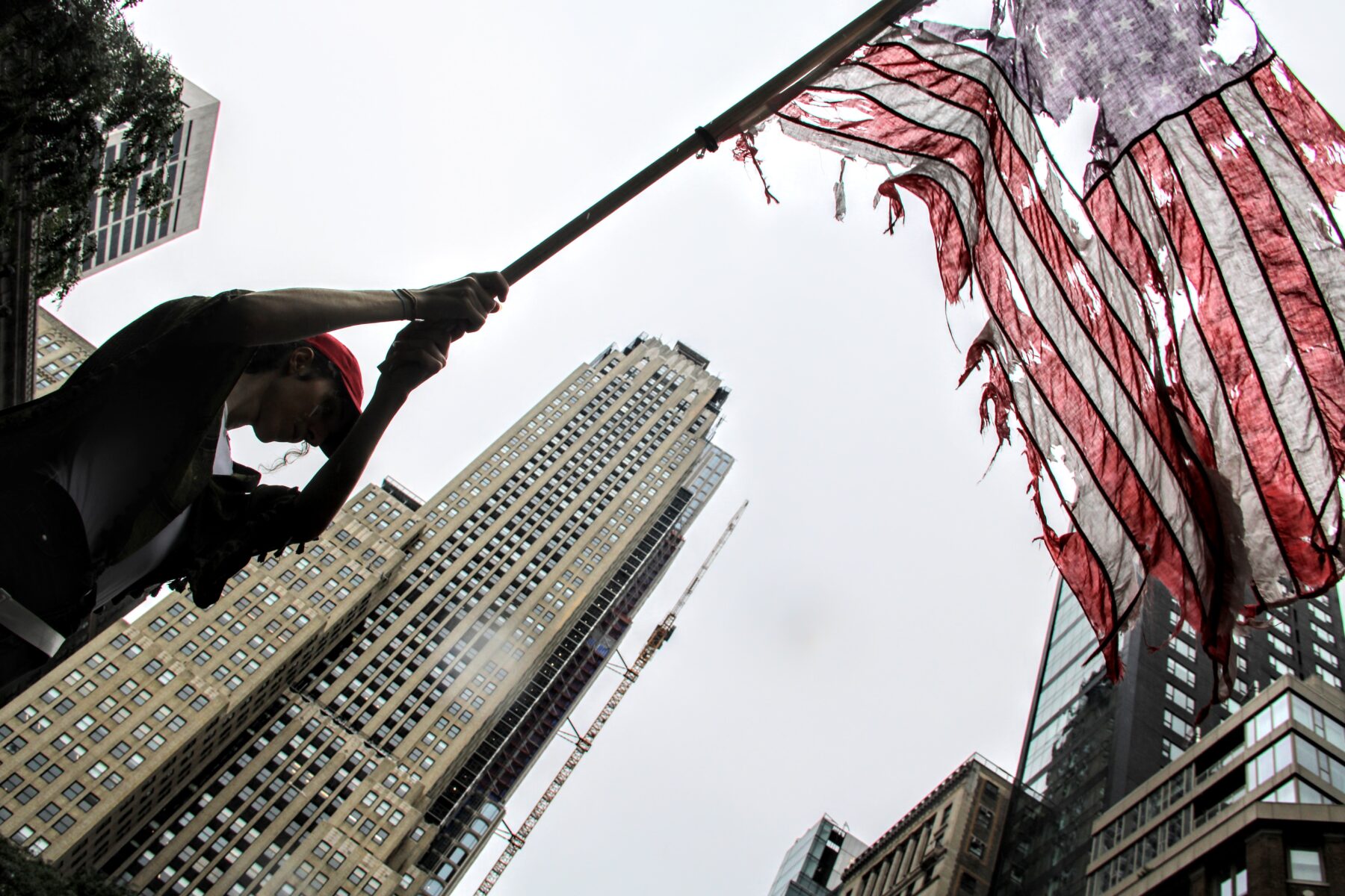 A demonstrator waves a tattered American Flag during the 'No Kings' Protest in New York City. (Credit: Abbie Hopson)