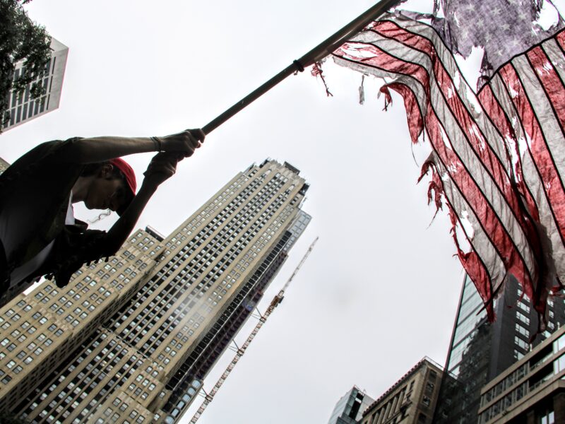 A demonstrator waves a tattered American Flag during the 'No Kings' Protest in New York City. (Credit: Abbie Hopson)