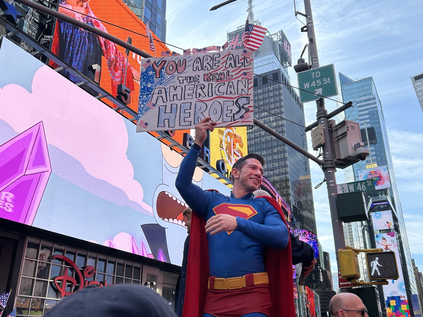 A man dressed as Superman at Saturday’s “No Kings” Protest in Times Square, holding up a sign reading “You Are All The Real American Heroes." (Credit: Hannah Smith)