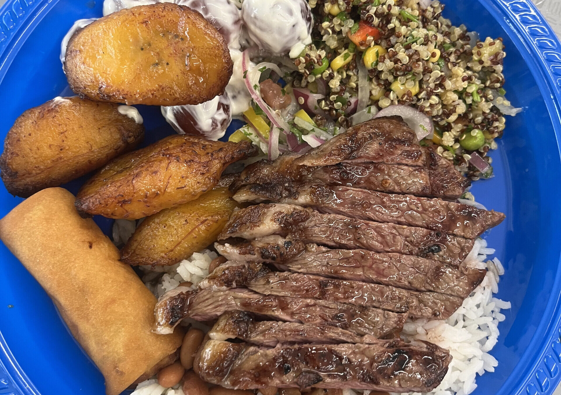 A plate from Rio Market’s buffet section featuring picanha﻿, a popular Brazilian grilled beef cut, served with white rice, beans, quinoa salad, fried plantains, and more. (Credit: Noa Metta)