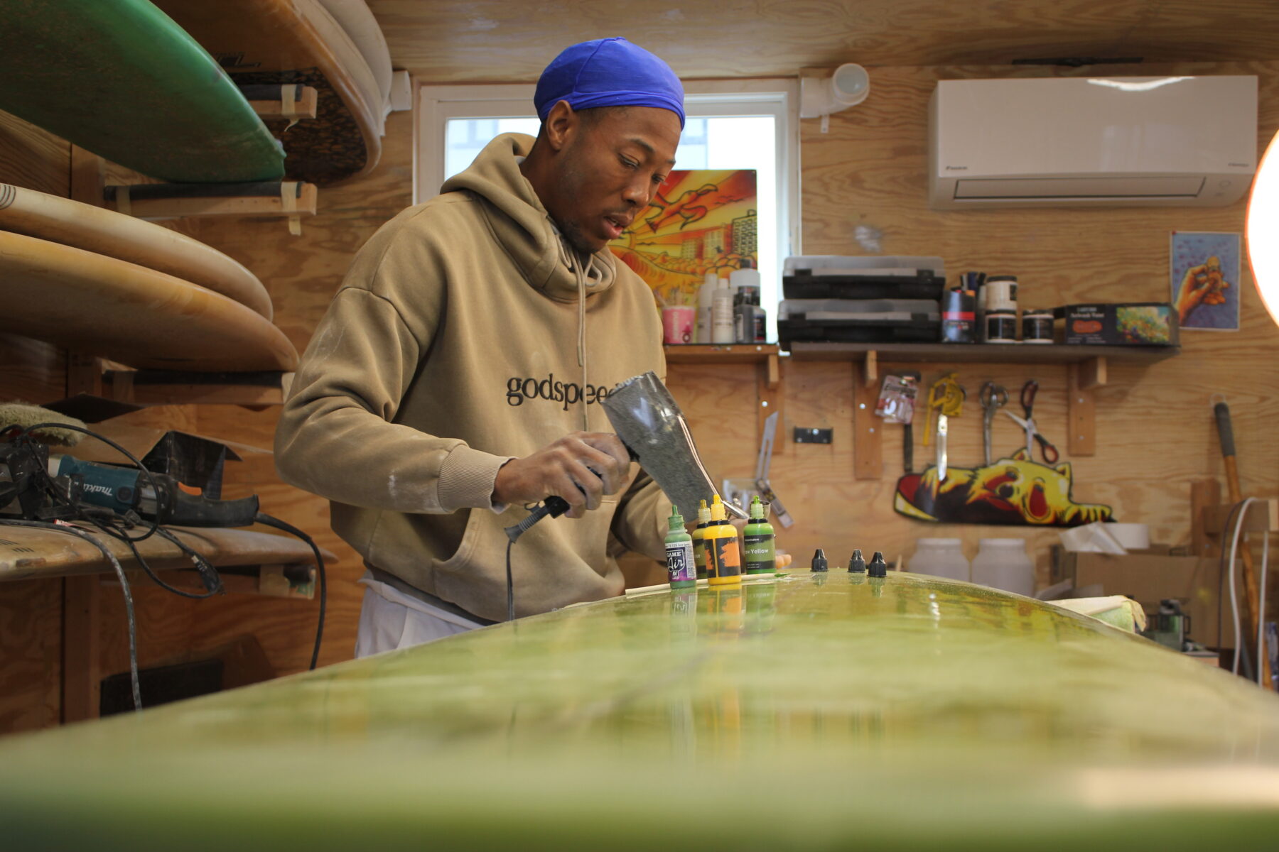 In his shipping-container workspace, Rockaway shaper Paul Godette repairs a dent in a client’s board, part of his effort to keep surfboards in use instead of tossed out. (Credit: Kate Waxman)